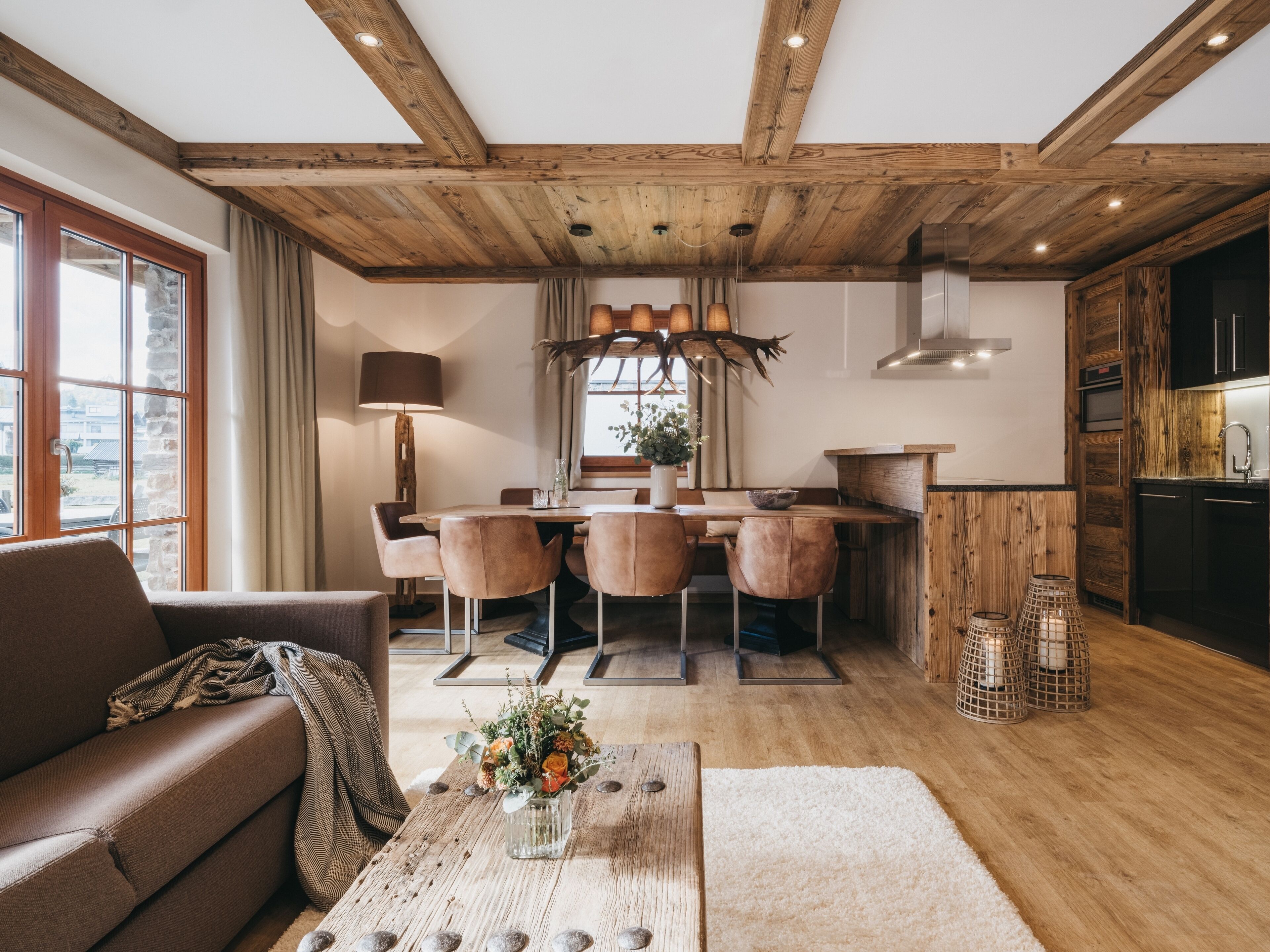 Een gezellige woonkamer met een houten plafond, een eethoek met een houten tafel en stoelen, en een keuken met houten kastjes en een fornuis.