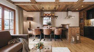 Ein gemütliches Wohnzimmer mit Holzboden, ein Essbereich mit Holztisch und -stühlen sowie eine Küche mit Holzschränken und Herd.