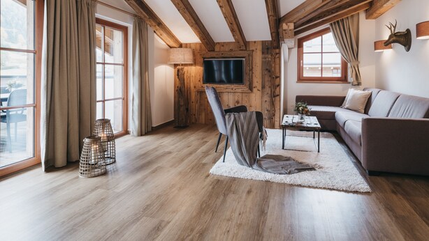 A spacious living room with wooden beams, a sofa, a TV, and a view of the outdoors. - VAYA Kaprun (Kaprun)