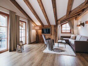 Amplia sala de estar con vigas de madera, un sofá, un televisor y vistas al exterior.
