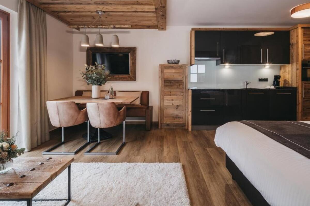 A cozy room with a wooden ceiling, a dining area with chairs, a bed, and a kitchen with dark cabinets and a wooden counter.