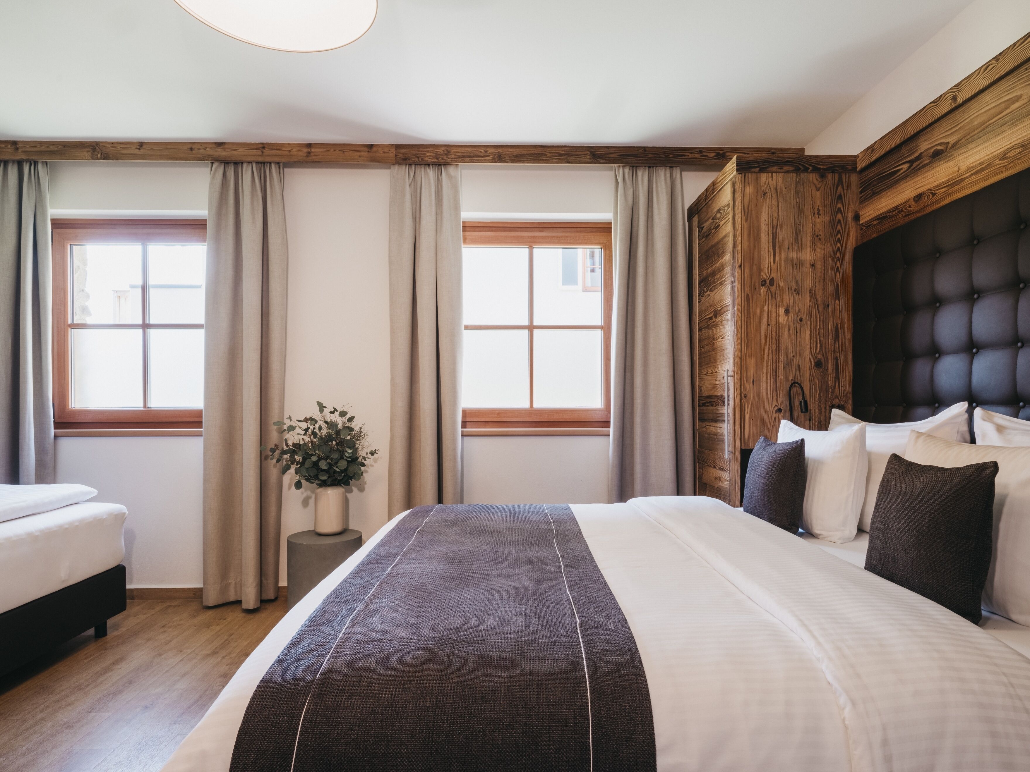 Une chambre à coucher avec un grand lit, une tête de lit en bois et deux fenêtres avec des rideaux.