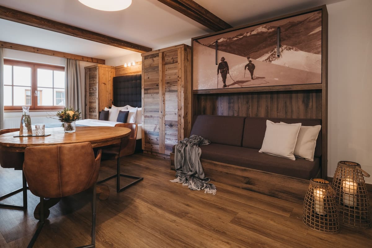 A cozy room with a wooden dining table, a sofa, and a bed with a wooden headboard.