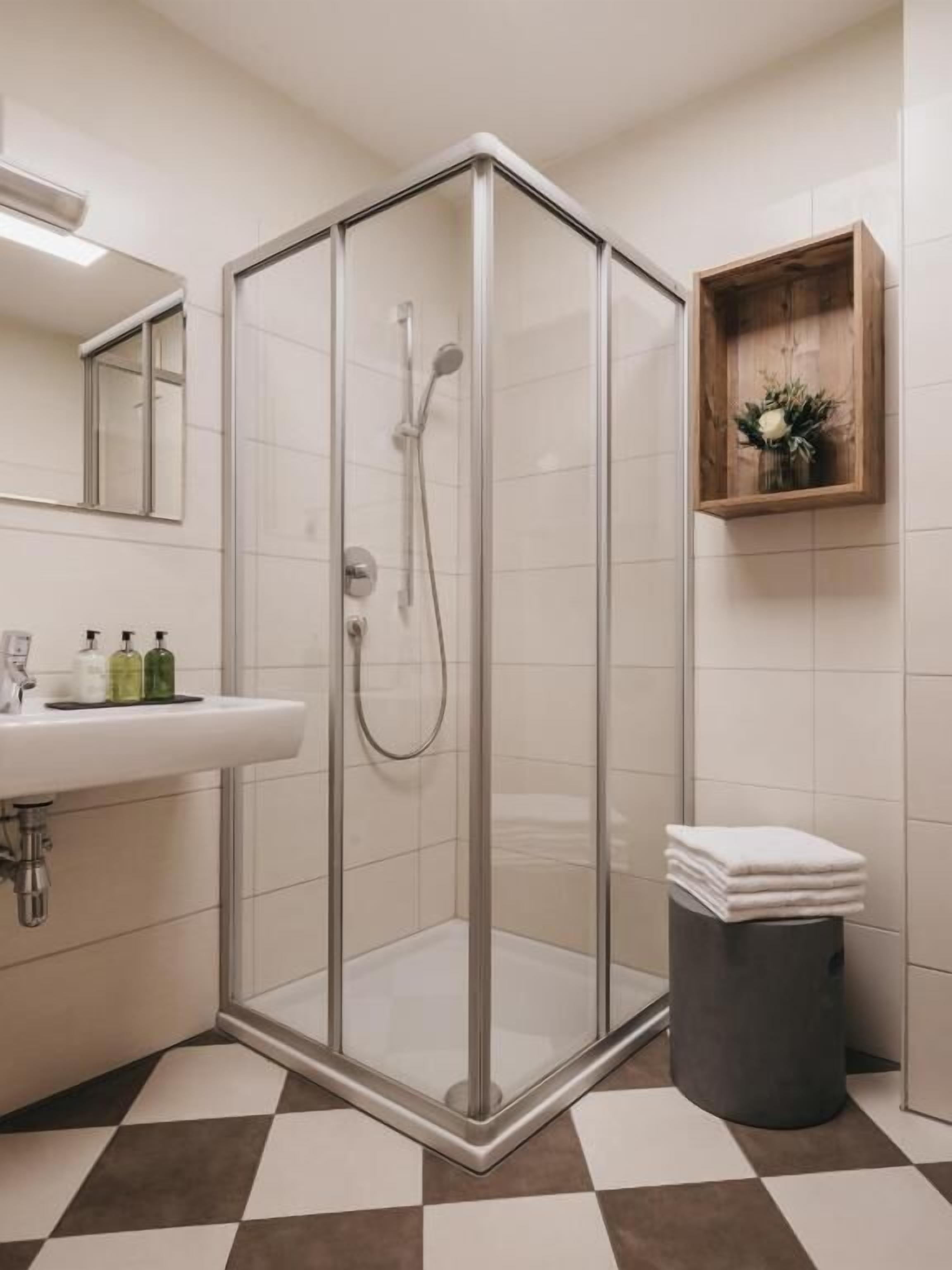 A modern bathroom with a glass-enclosed shower, a sink with toiletries, and a checkered floor.