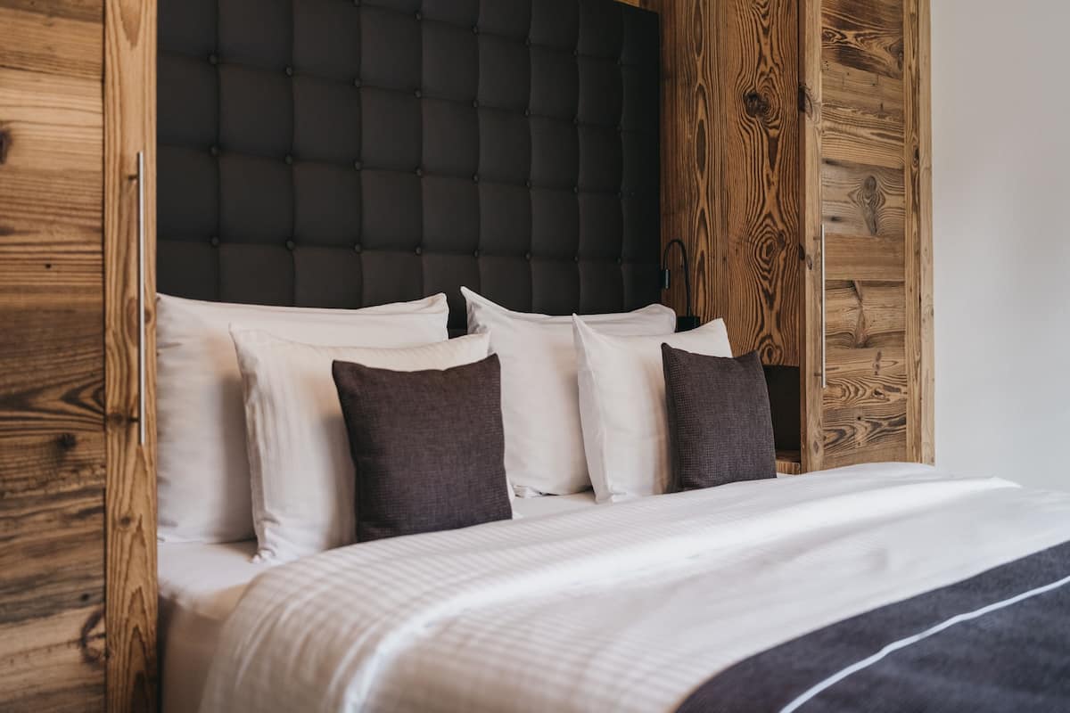 A bed with white and dark pillows, a dark tufted headboard, and wooden paneling on the walls.