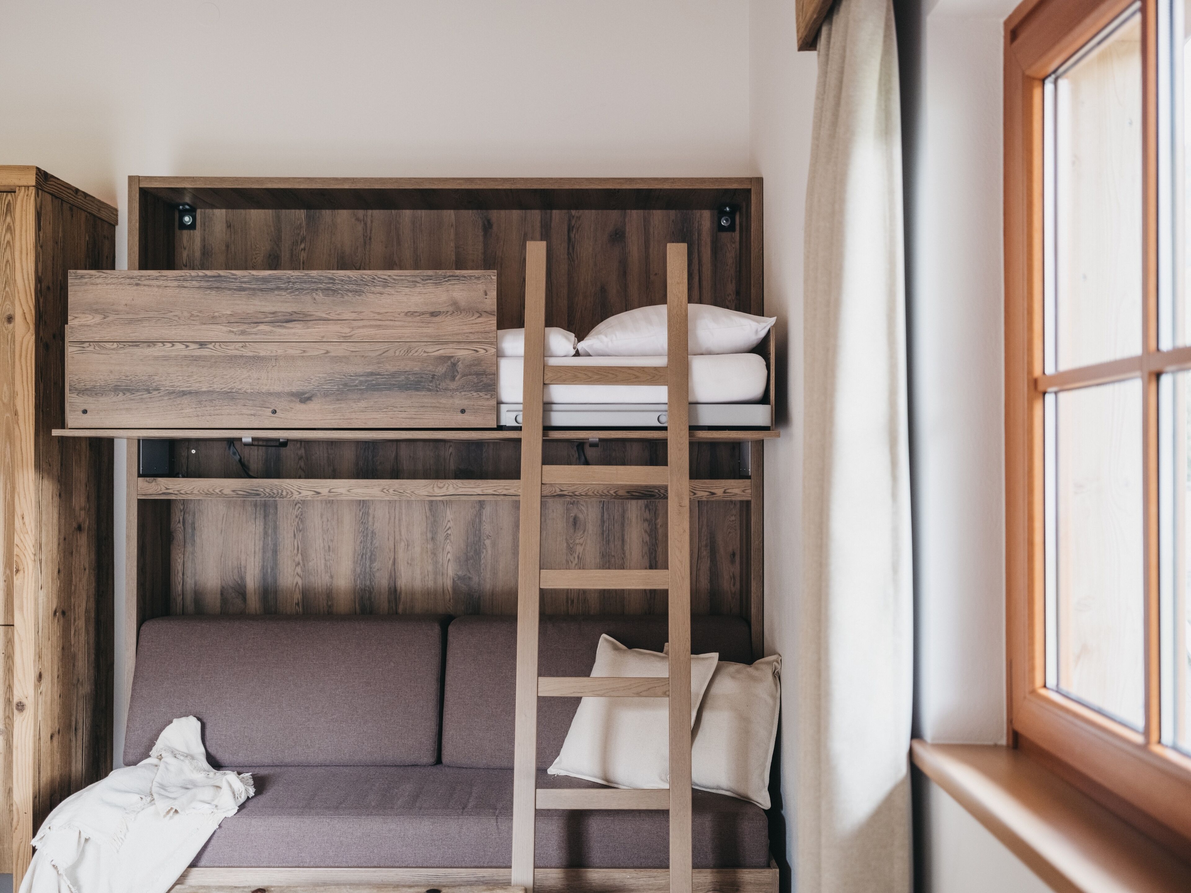 Una cama litera con escalera de madera, colchón gris y almohadas blancas.