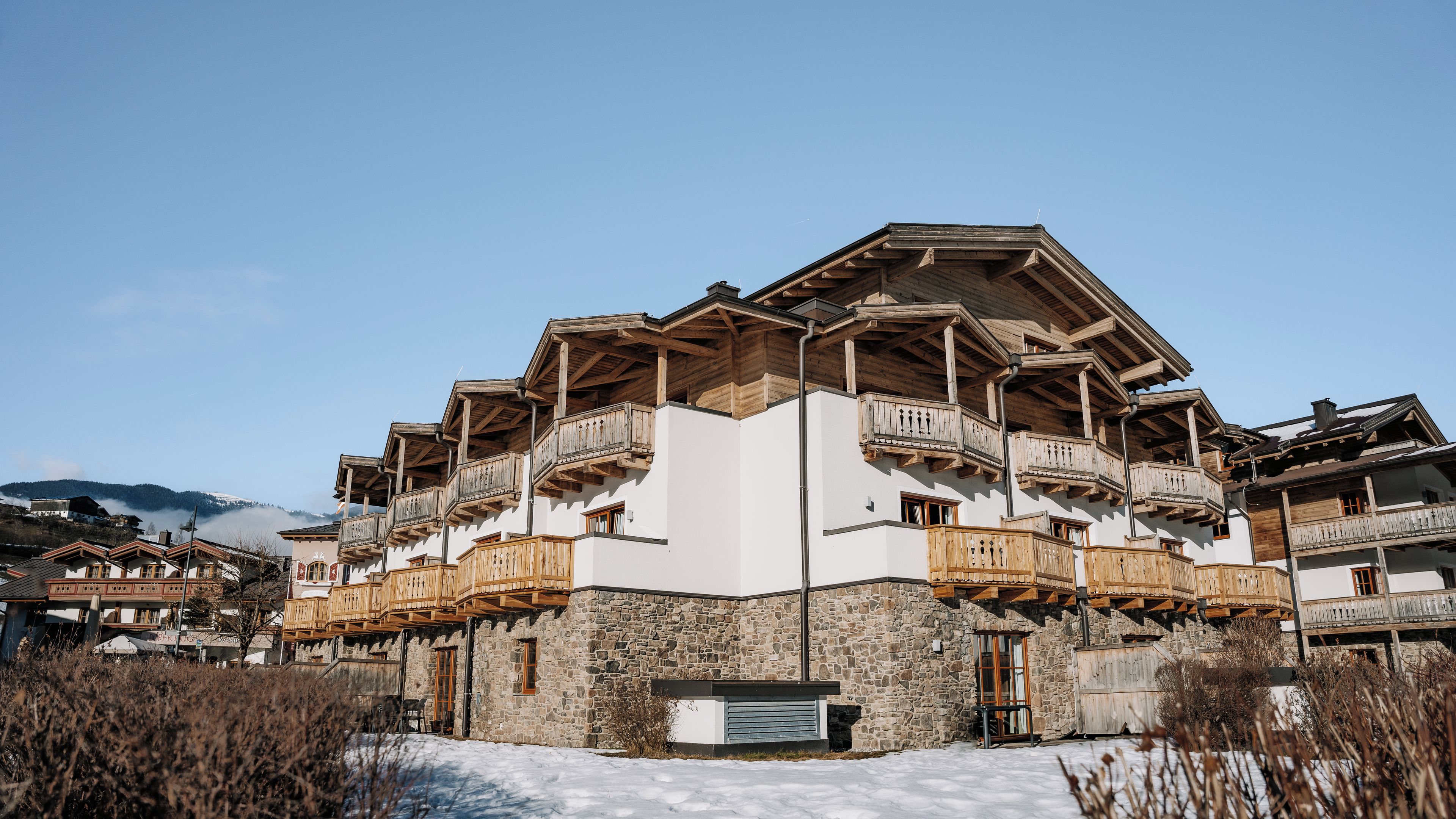 A multi-story building with wooden balconies and stone walls, surrounded by snow.
