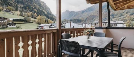 A wooden deck with a table and chairs, overlooking a mountainous landscape with buildings in the distance.