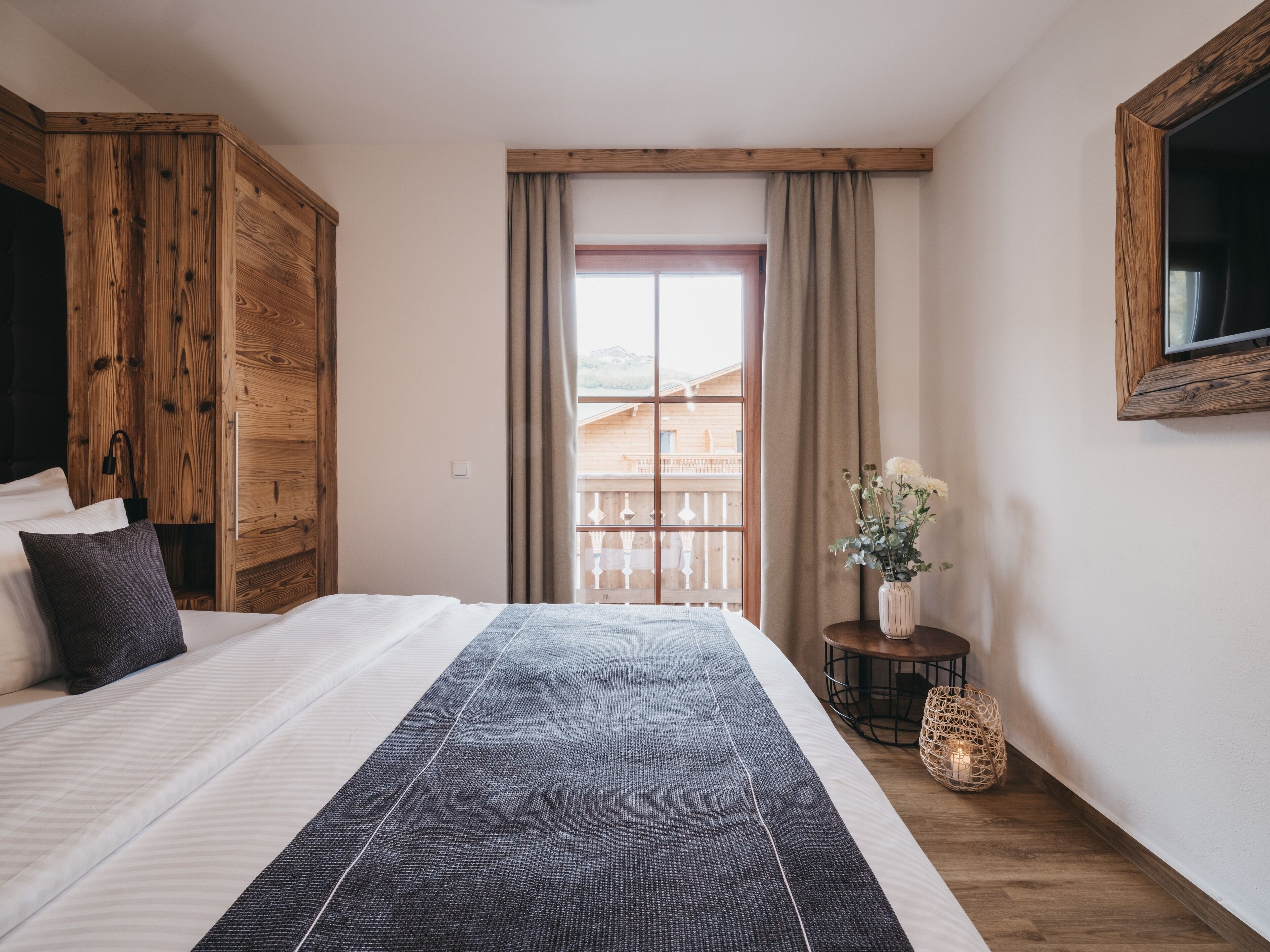 A bedroom with a large bed, wooden wardrobe, and a window with curtains.