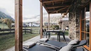 A covered outdoor seating area with lounge chairs and a table, overlooking a mountainous landscape. - VAYA Kaprun (Kaprun)