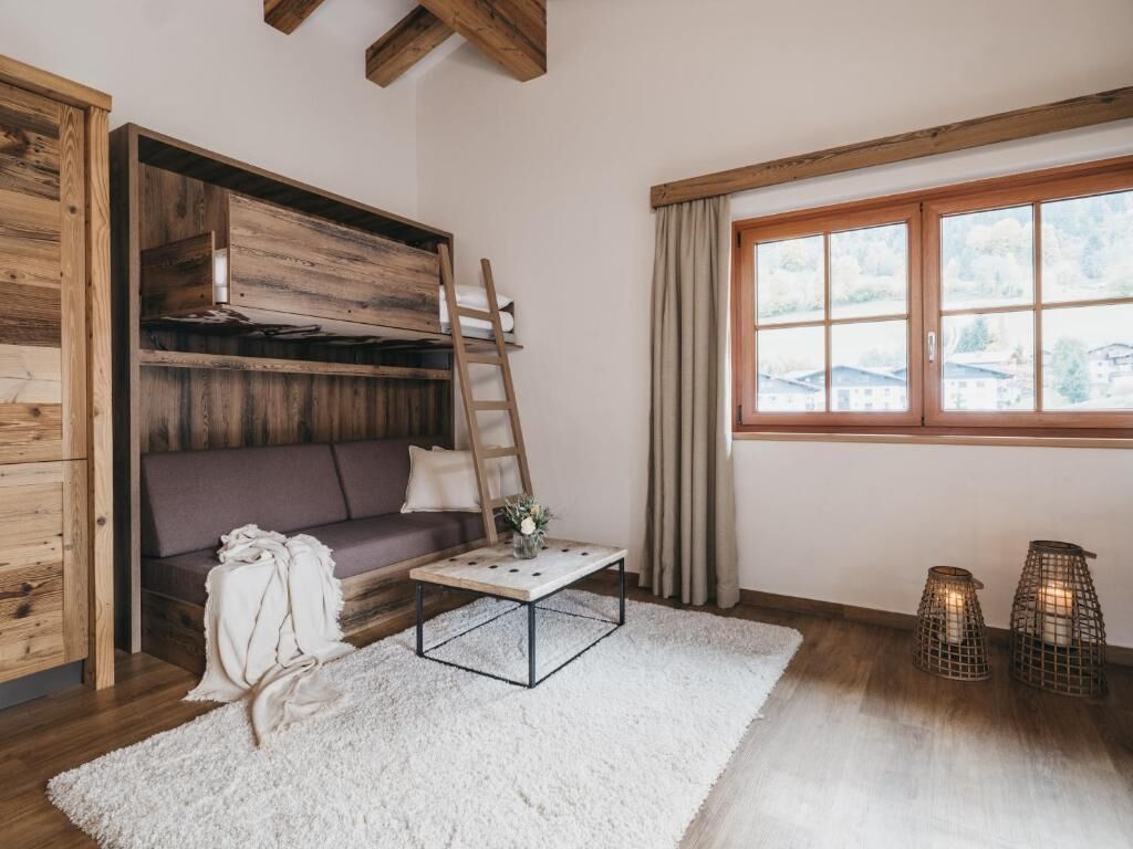Ein gemütliches Zimmer mit einer Holzwand, einem Sofa, einem Couchtisch, einer Himmelsleiter, einem Fenster mit Vorhängen und zwei Wandleuchten.