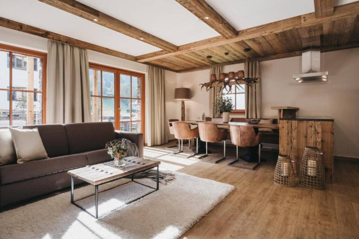 A modern living room with a wooden ceiling, a sofa, a coffee table, and a dining area with chairs and a table.