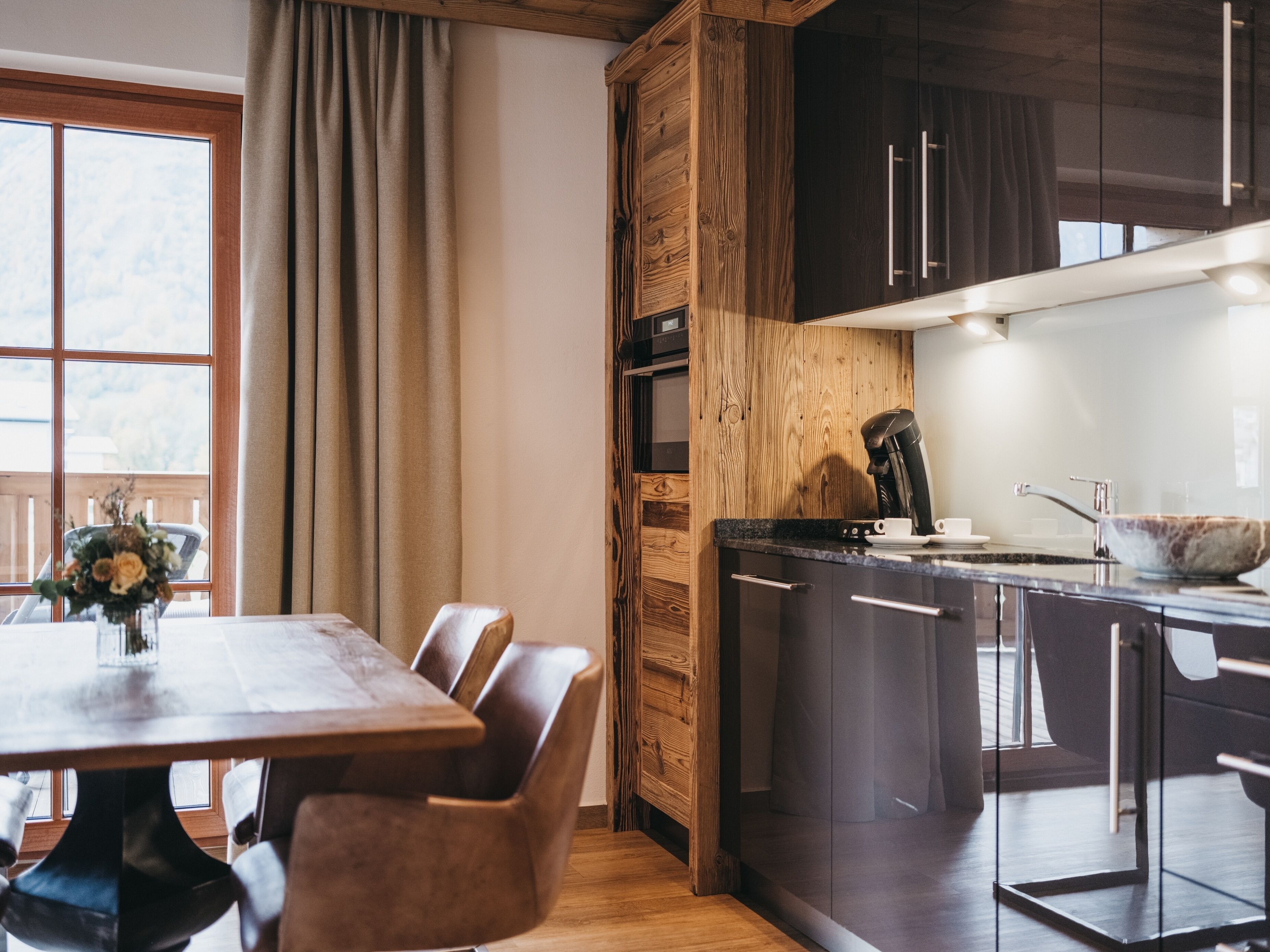 Una cucina moderna con mobili scuri, una parete d'accento in legno e un'area pranzo con tavolo e sedie.
