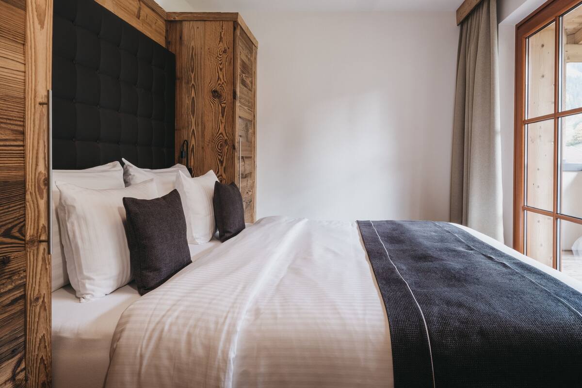 A bedroom with a bed, wooden headboard, and a large window.