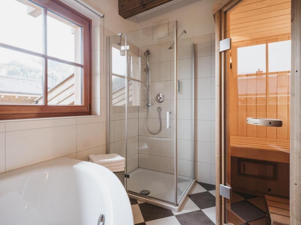 A modern bathroom with a glass-enclosed shower, a white bathtub, and a wooden door.