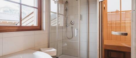 A modern bathroom with a glass-enclosed shower, a white bathtub, and a wooden door.