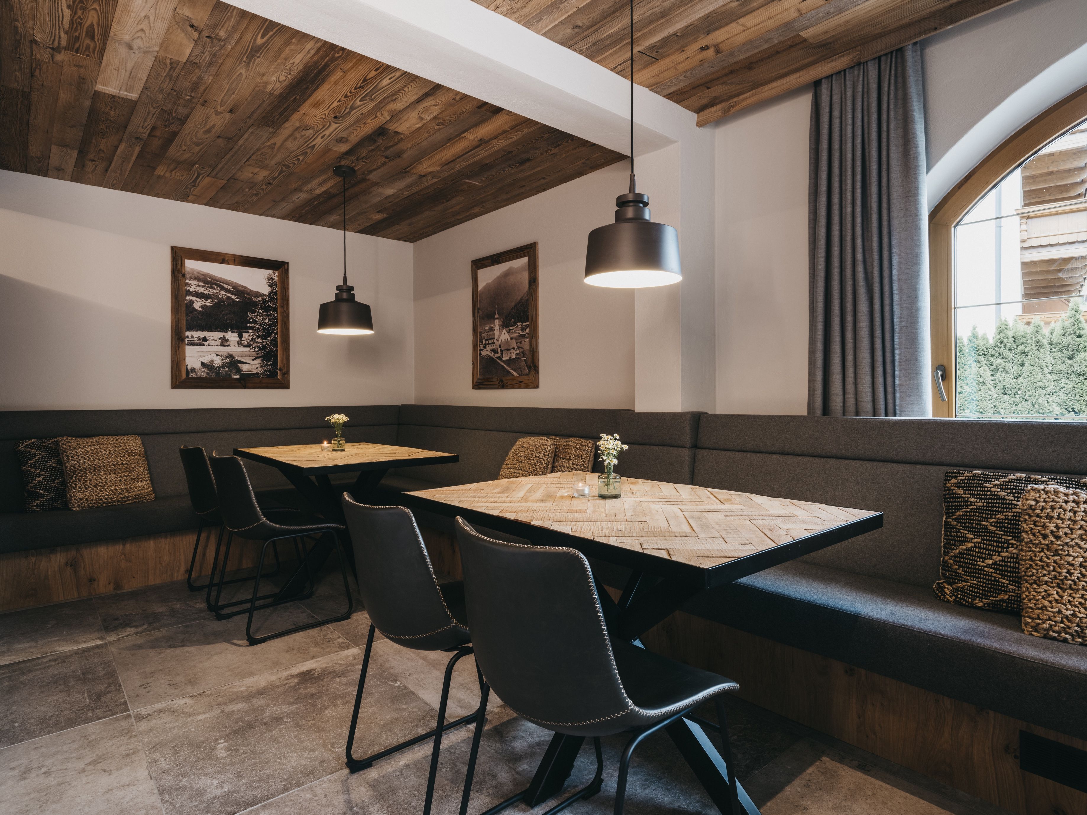 Un espace repas doté d’un plafond en bois, de deux suspensions lumineuses, d’une table avec des chaises et d’un banc agrémenté de coussins.