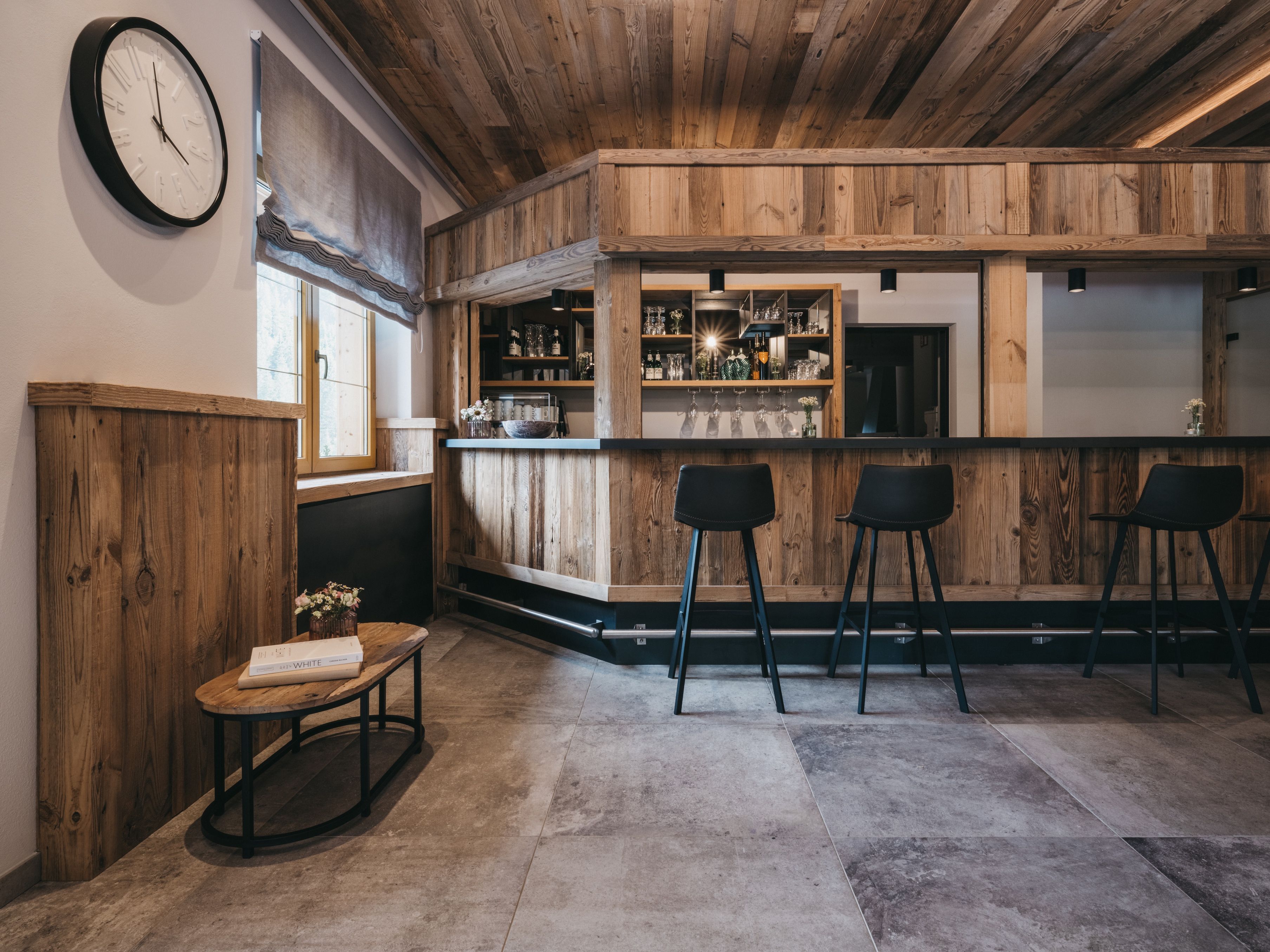 Un coin bar avec des lambris en bois, une horloge au mur et des tabourets de bar.