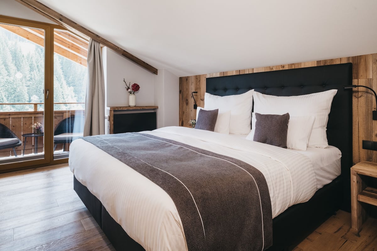 A bedroom with a large bed, wooden headboard, and a view of a balcony with a wooden railing.