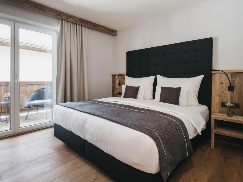 A bedroom with a large bed, a wooden headboard, a nightstand, and a sliding glass door leading to an outdoor area.
