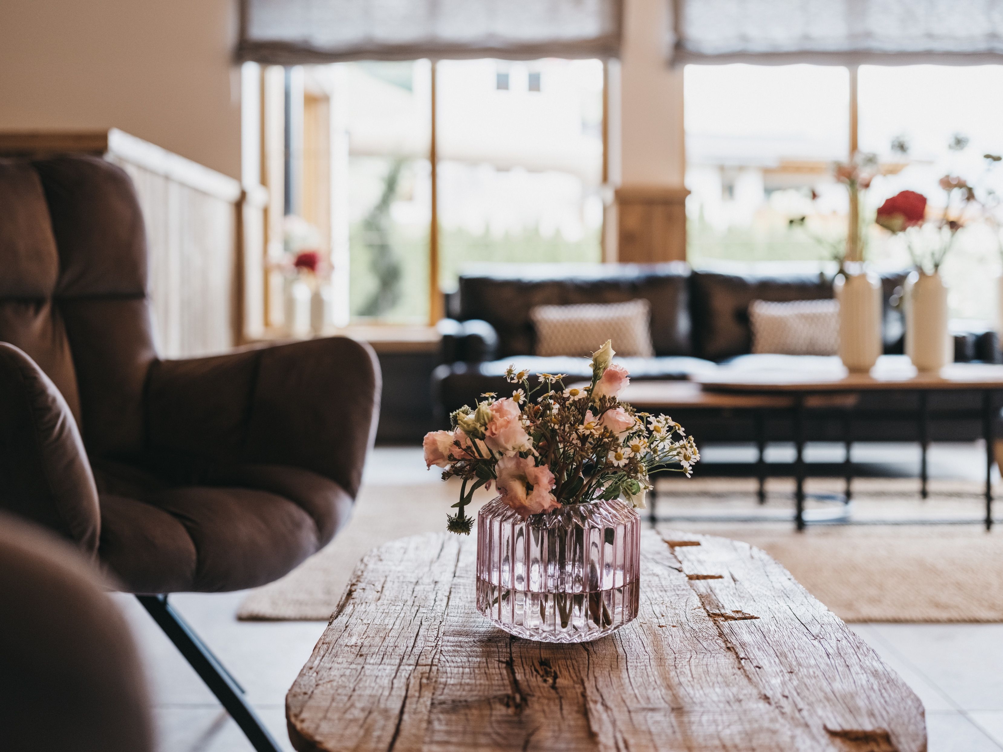 A room with a wooden coffee table, a brown leather chair, and a vase with flowers.