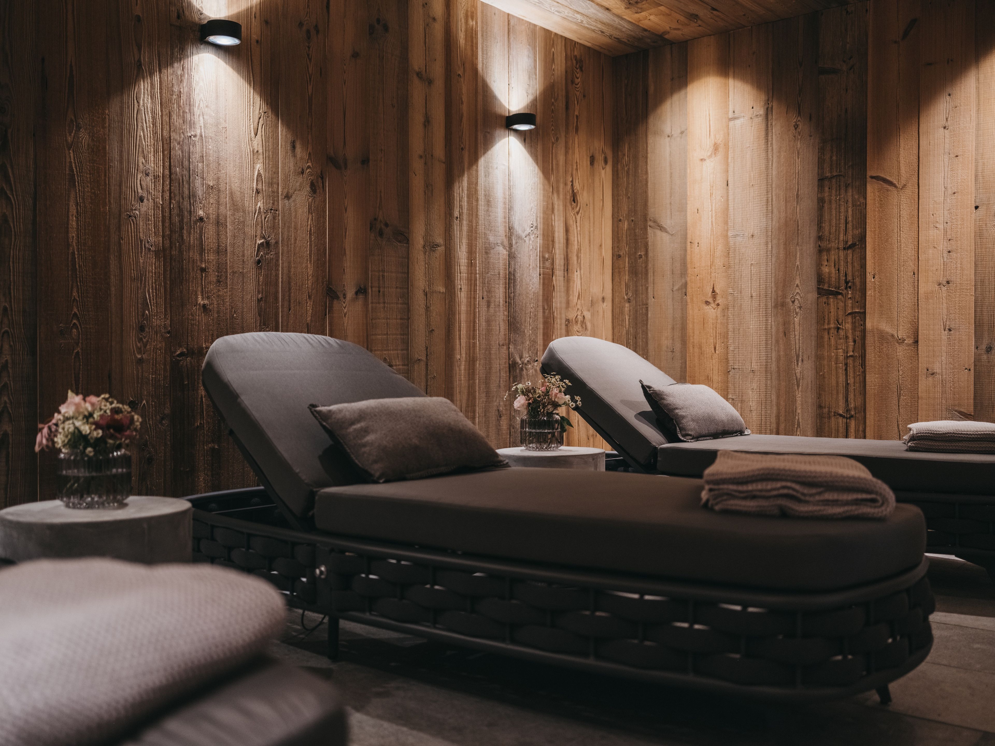 Un cuarto de spa con paredes de madera, dos sillones reclinables, una mesita con un florero y una lámpara fijada a la pared.