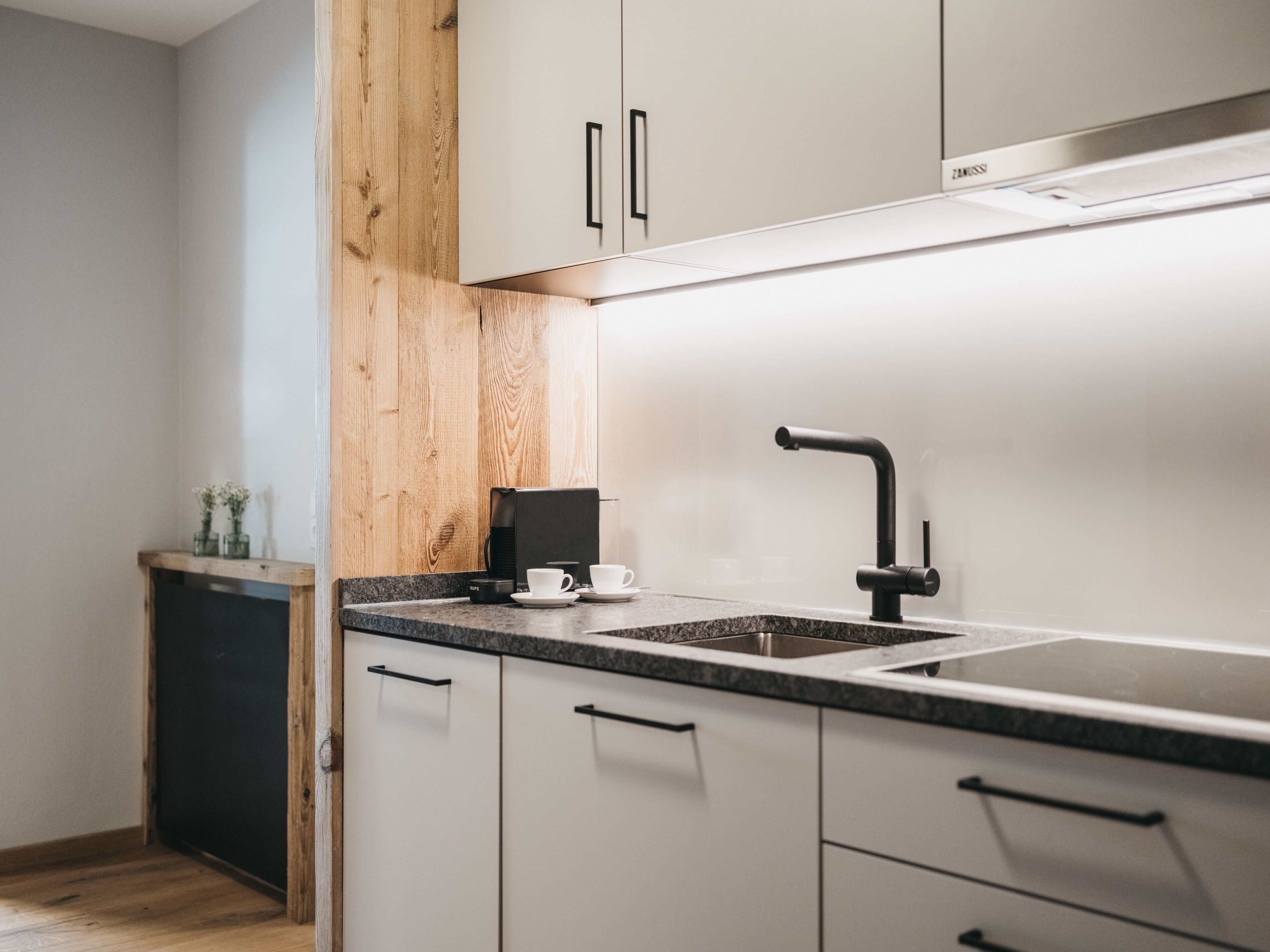 Een moderne keuken met witte kastjes, een zwarte koffieapparaat en een roestvrijstalen spoelbak.