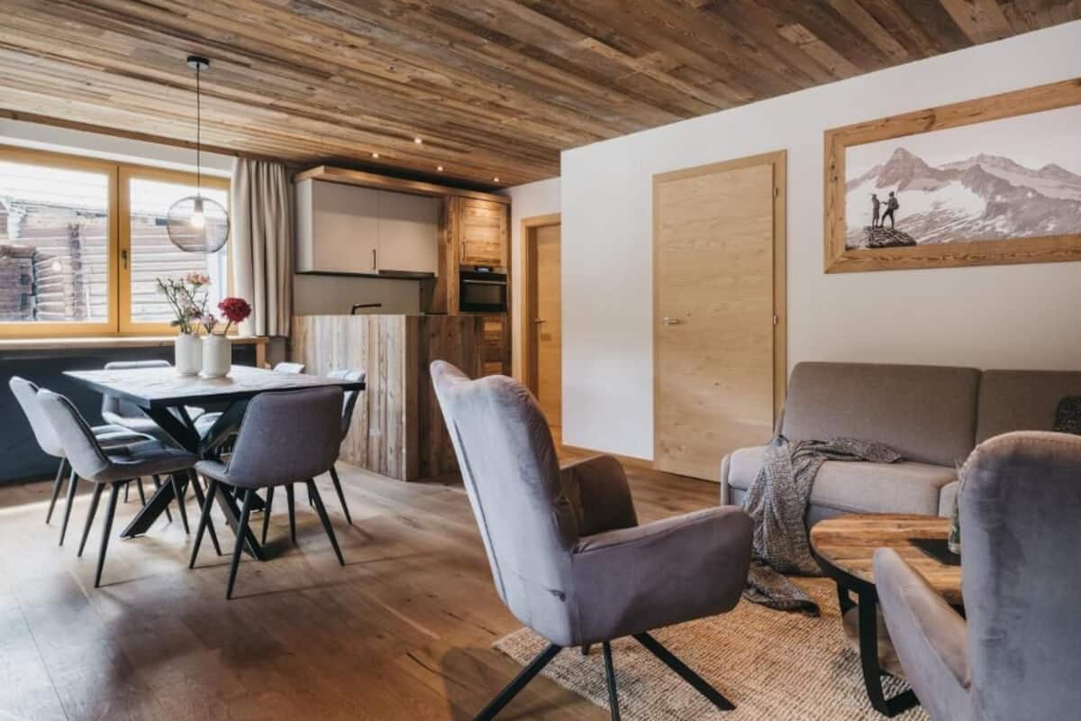 A modern interior with a wooden ceiling, a dining area with a table and chairs, a sofa, and a painting on the wall.