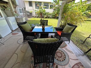 An outdoor patio with a table and chairs, surrounded by a garden and a building in the background. - Discover a captivating home nestled in the vibrant heart of Hilo. (Hilo)