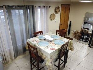 A dining area with a table set for four, surrounded by chairs, and a kitchen area visible in the background. - Discover a captivating home nestled in the vibrant heart of Hilo. (Hilo)