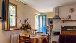 Un comedor con una mesa dispuesta para dos personas, un florero con flores y una cocina al fondo.