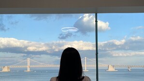 Une personne assise près d’une fenêtre donnant sur un pont et la mer.