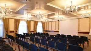 A conference room with rows of black chairs, large windows with curtains, and chandeliers. - Riviera on Vaal Resort (Vereeniging)