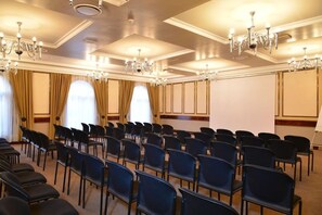 Una sala de conferències amb files de cadires negres, grans finestres amb cortines i lluminàries penjants.