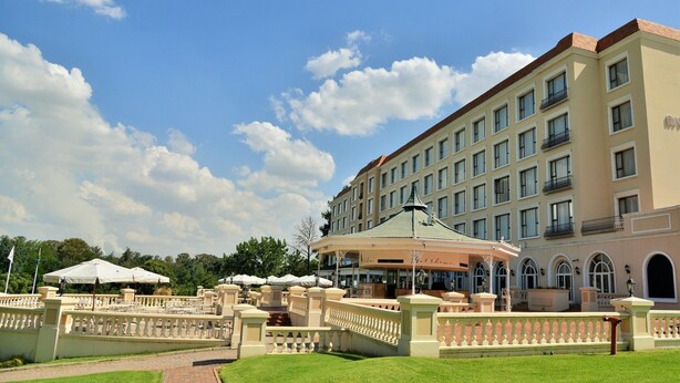 A hotel with a large building, a covered area with umbrellas, and a well-maintained garden. - Riviera on Vaal Resort (Vereeniging)
