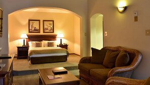 A hotel room with a bed, two bedside lamps, a small table, a wicker armchair, and a mirror. - Riviera on Vaal Resort (Vereeniging)