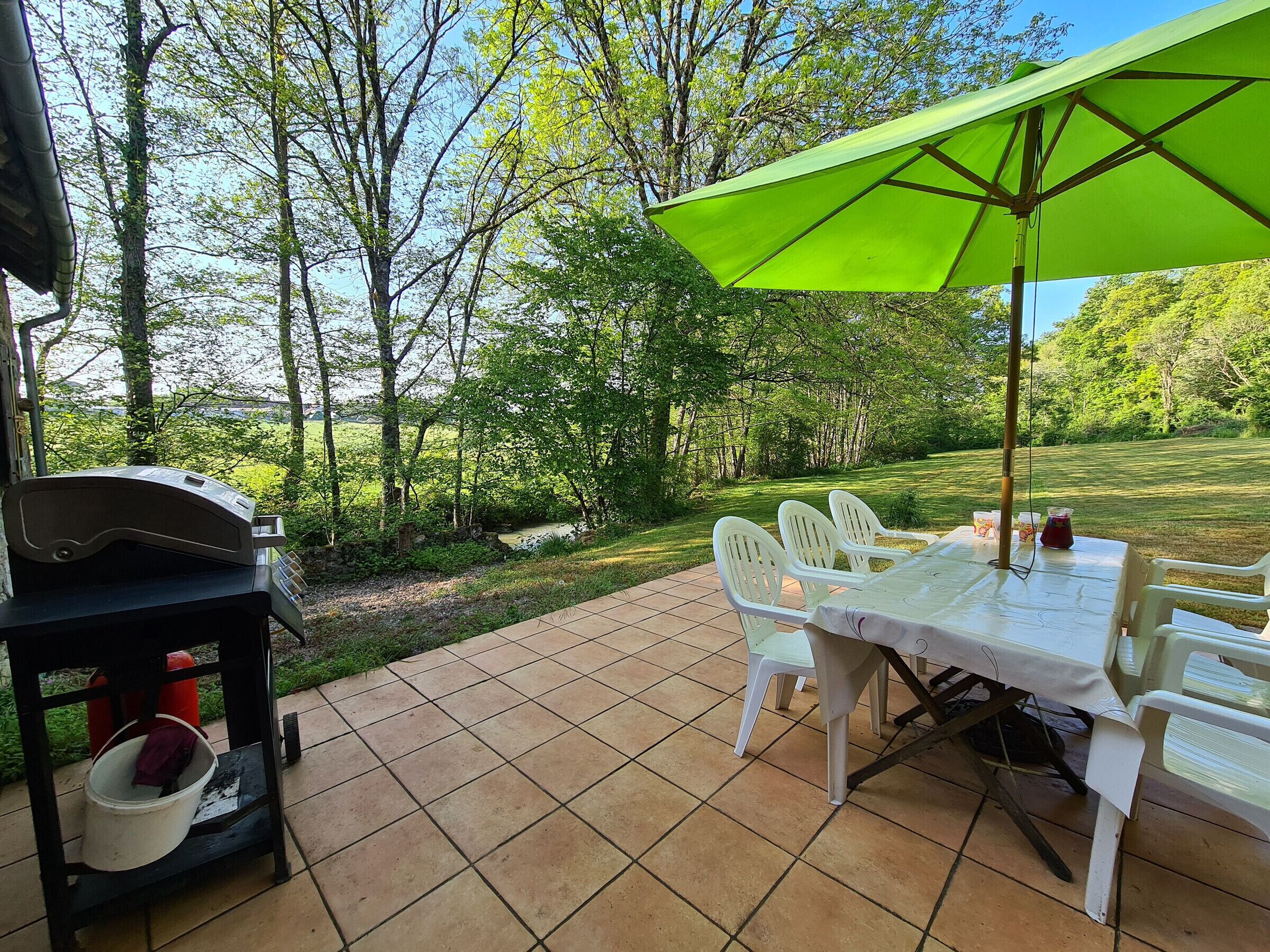 An outdoor patio with a grill, table, chairs, and a green umbrella.