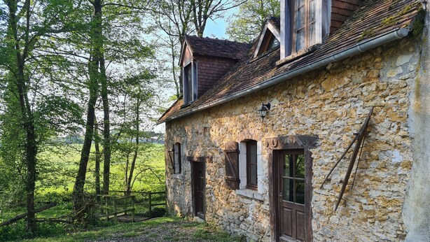 Un bâtiment rustique en pierre, doté d’un toit en pente, de volets en bois et d’un chemin de gravier menant à l’entrée.