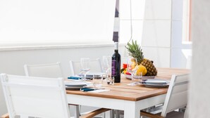 Een eettafel gedekt met witte stoelen, een fles wijn, glazen en een schaal fruit.