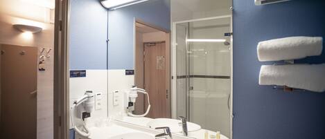 A hotel bathroom with two sinks, a mirror, and a glass shower enclosure.