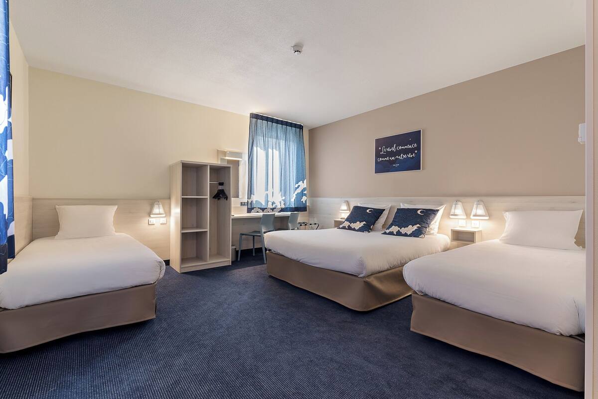 Une chambre d’hôtel avec deux lits, un bureau, une chaise et une armoire.