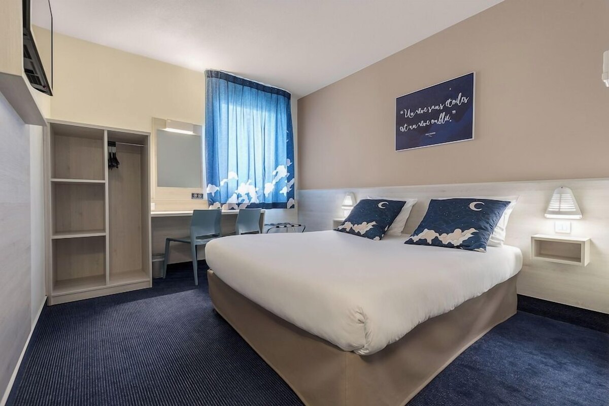 A hotel room with a bed, a desk, a chair, a wardrobe, and a window with curtains.