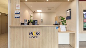 A hotel reception desk with a wooden finish, a digital screen, and a sign indicating no smoking.