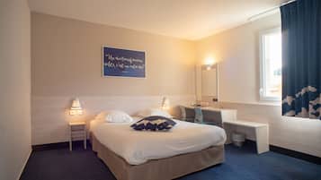 Una habitación de hotel con cama, mesitas de noche, escritorio, espejo y ventana con cortinas.
