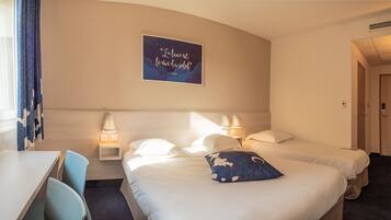 Une chambre d’hôtel avec deux lits, un bureau et une chaise. Il y a une affiche au mur et deux lampes de chevet.