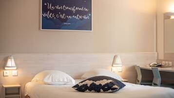 A hotel room with a bed, two bedside lamps, a desk, and a wall-mounted quote.