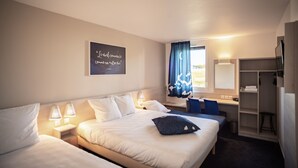 A hotel room with two beds, a desk, a chair, a wardrobe, and a window with curtains.
