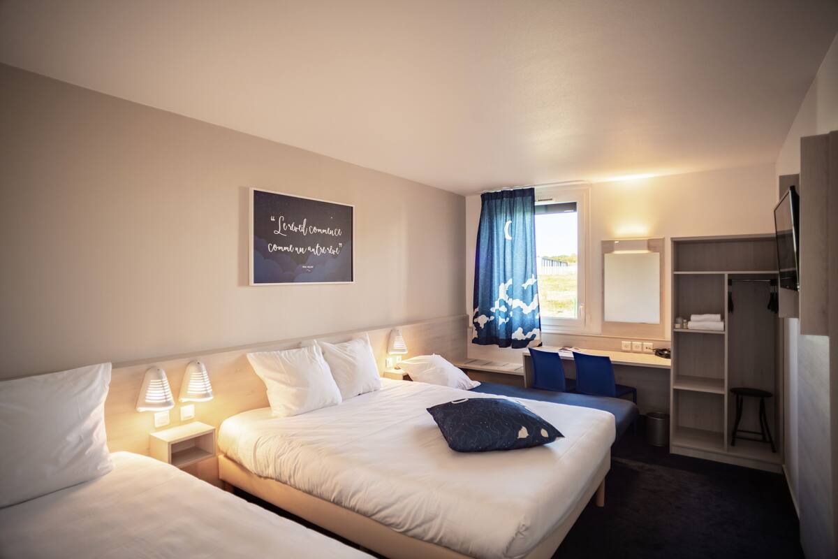 Une chambre d’hôtel avec deux lits, un bureau, une chaise, une armoire et une fenêtre avec des rideaux.