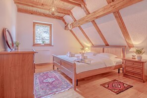 A bedroom with a sloped ceiling, wooden beams, a bed, bedside tables, a nightstand, a radiator, a window, and a mirror. - Chalet Primus in Soca Valley (Bovec)