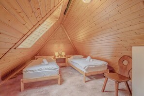 A small, wooden, attic-style room with two beds, a chair, and a nightstand.